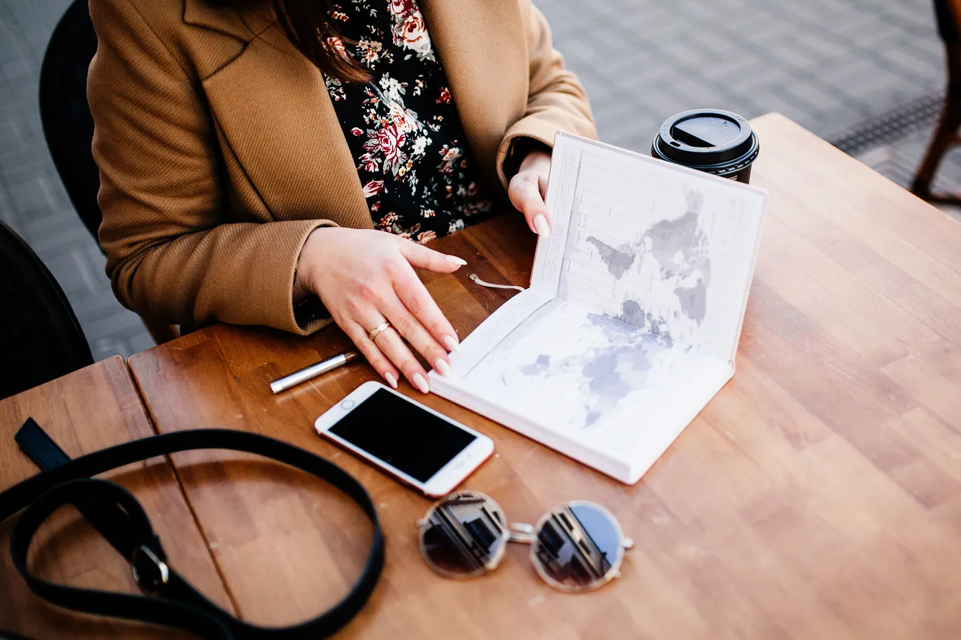 Planning a trip at a cafe table with an open world-map notebook and coffee